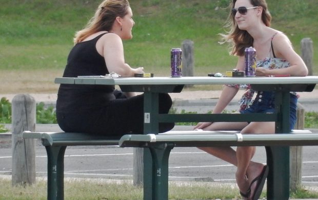 Dos amigas conversando junto a una mesa al aire libre. Fotografía referencial.